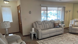 A living room with a beige sofa, a patterned rug, and a window with a view of a parking lot. - Serene 3-bedroom house in Sun City
Golf course & lake front near Stadium. (Sun City)