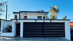A modern two-story house with a large black garage door, a balcony, and a clear blue sky.