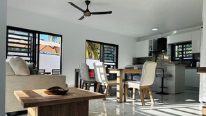 A modern kitchen with white cabinets, a dining area with a wooden table and chairs, and a ceiling fan.