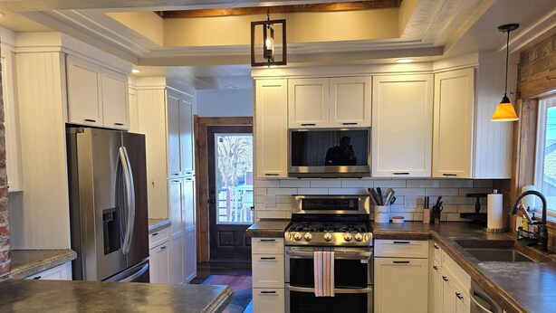 A modern kitchen with white cabinets, stainless steel appliances, and a wooden floor. - Charming Bungalow • Hot Tub • Near Trails & Dining (Ogden)
