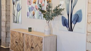 A hallway with wooden herringbone-patterned cabinets, a vase with green foliage, and two large floral paintings on the wall. - Charming Bungalow • Hot Tub • Near Trails & Dining (Ogden)