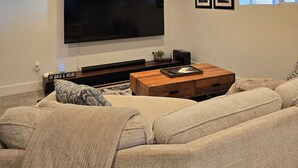 A living room with a large flat-screen TV mounted on the wall, a wooden coffee table, and a beige sofa. - Charming Bungalow • Hot Tub • Near Trails & Dining (Ogden)