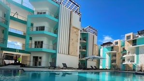Ein modernes Gebäude mit Schwimmbad, mehreren Balkonen und blauem Himmel.