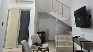 Ein großzügiger Wohnbereich mit hoher Decke, einer Treppe zu einer oberen Ebene, einem Flachbildfernseher und einem modernen Design.