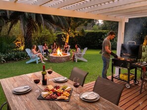 An outdoor patio with a wooden table set for a meal, a fire pit, and a grill. - Swannie Creek - Private Hot Tub Retreat in the Elgin Valley! (Grabouw)