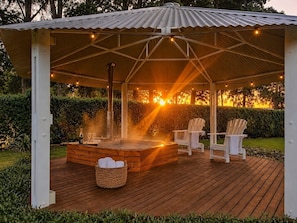 Una terraza de madera con un jacuzzi, dos sillas Adirondack y un pabellón cubierto.