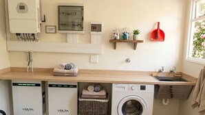 A laundry room with a washing machine, two dishwashers, a utility meter, and a window with flowers.