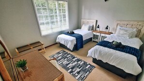 A bedroom with two beds, a small table, a chair, a window with blinds, and a wall-mounted shelf. - Swannie Creek - Private Hot Tub Retreat in the Elgin Valley! (Grabouw)