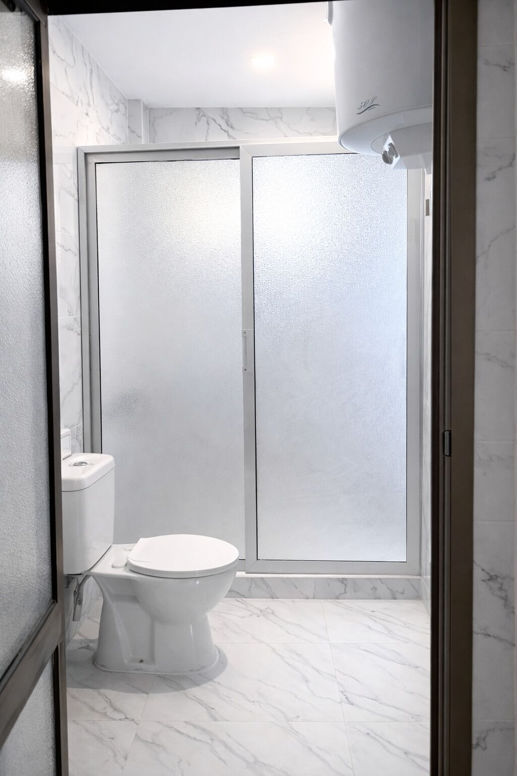 A bathroom with a toilet, a shower enclosure, and marble flooring.