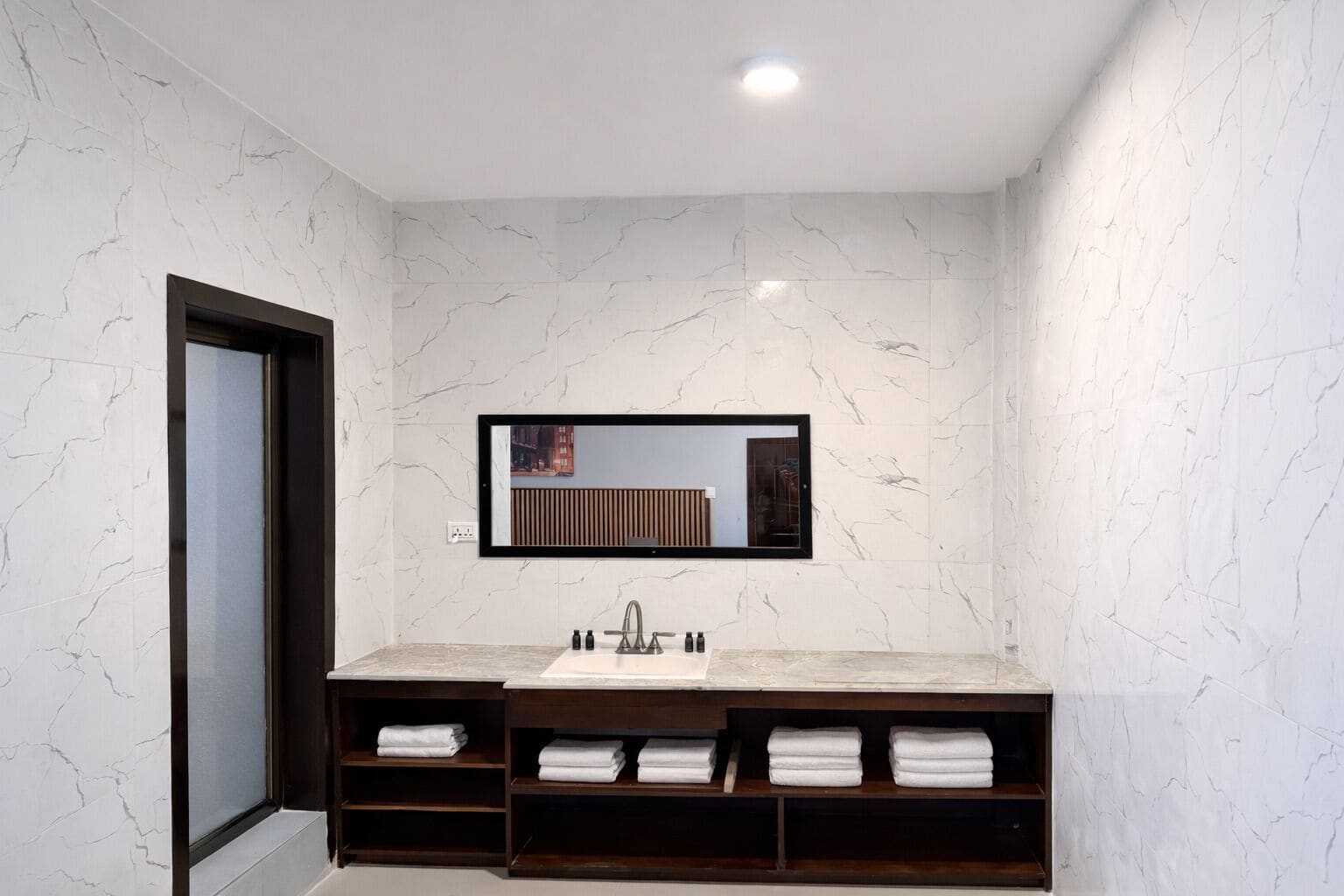 Een moderne badkamer met een marmeren wand, een grote spiegel, een wastafel en inbouwkasten voor handdoeken.