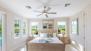Ein Schlafzimmer mit einem großen Bett, zwei Nachttischen, einem Deckenventilator und großen Fenstern.