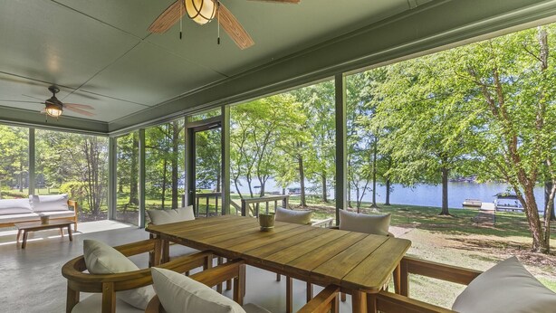 Mesa de jantar de madeira com cadeiras, janelas amplas e vista para um lago.