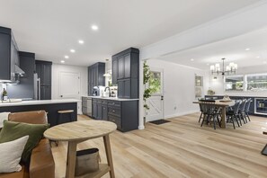 A modern kitchen with dark cabinets, a central island, and a dining area with a round table and chairs.