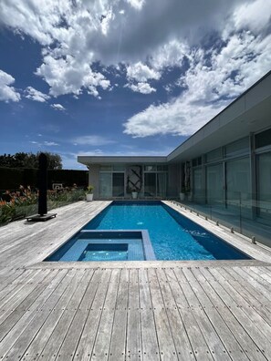 A modern house with a rectangular swimming pool surrounded by a wooden deck.
