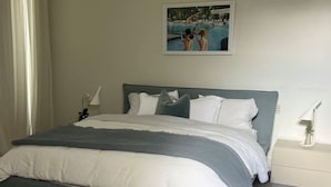 A neatly made bed with a grey and white color scheme, a framed picture on the wall, and a bedside table with a lamp. - Portsea Paramount - when only the best will do! (Portsea)