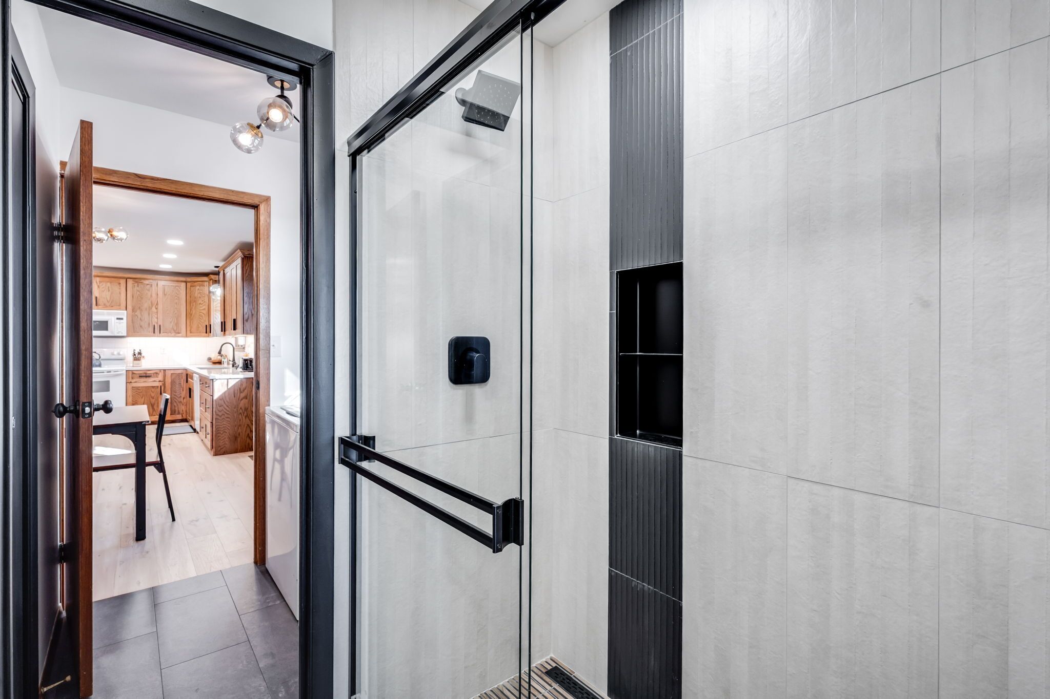 Une salle de bain moderne avec une porte de douche en verre, un porte-serviettes noir et une pomme de douche bien visible.