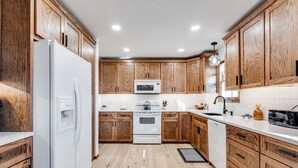 Une cuisine avec des meubles de rangement en bois, un réfrigérateur blanc, un four à micro-ondes, un four traditionnel et un lave-vaisselle.