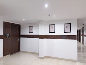 Een hotellobby met een houten deur met het nummer '305', een betegelde vloer en drie ingelijste foto's aan de muur.