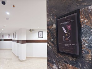 Zona de recepción de hotel con pared de mármol, obras de arte enmarcadas y un cartel con el nombre y la ubicación del hotel.