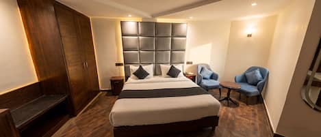 Une chambre d’hôtel avec un grand lit, une armoire, un coin salon avec deux fauteuils et une petite table.