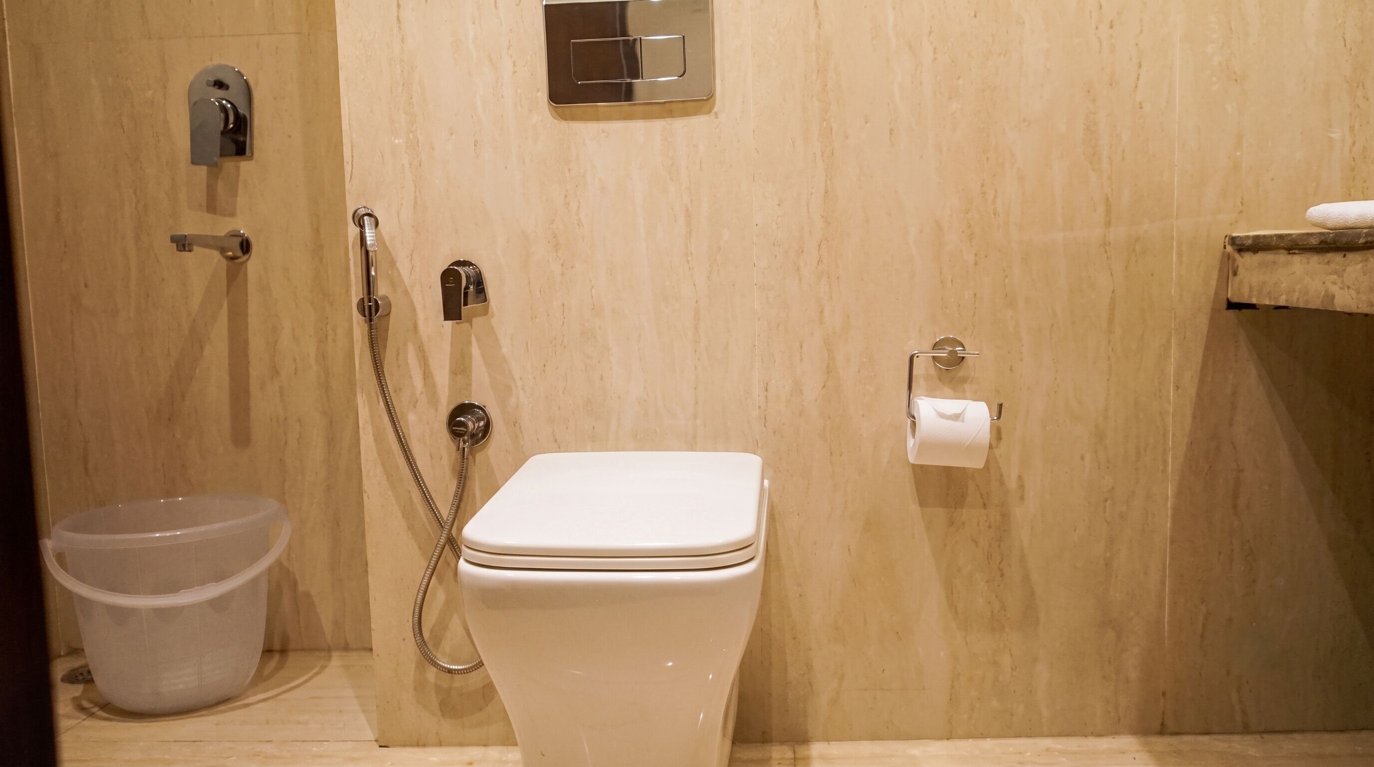 Un baño con inodoro, ducha, bidé, dispensador de papel higiénico y un cubo de basura.