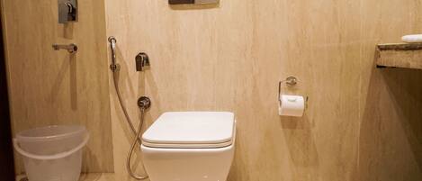 Un baño con inodoro, ducha, bidé, dispensador de papel higiénico y un cubo de basura.