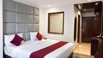 Una habitación de hotel con una cama grande, un cabecero gris, una puerta de madera y una obra de arte enmarcada en la pared.