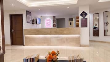 A hotel reception area with a reception desk, framed artwork, a digital display, and a floral arrangement.