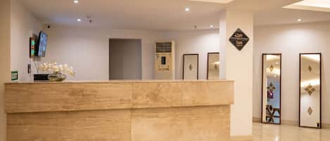 Un mostrador de recepción con un televisor de pantalla plana, un jarrón con flores y un equipo de aire acondicionado de pared.