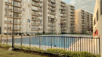 A residential building with multiple balconies, a swimming pool, and a fenced area.