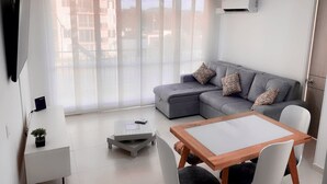 A modern living room with a grey sofa, a wooden coffee table, and a white TV stand. - Cozy 2-bedroom apartment in gorgeous Ricaurte with AC and gym (Ricaurte)