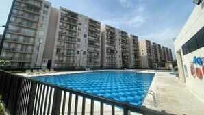 A swimming pool with a blue checkered pattern, surrounded by a black fence. In the background, there are multi-story residential buildings with balconies. - Cozy 2-bedroom apartment in gorgeous Ricaurte with AC and gym (Ricaurte)