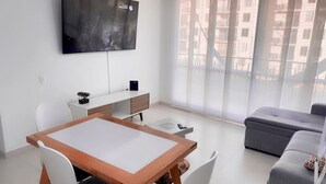 A modern living room with a dining table, white chairs, a grey sofa, and a TV mounted on the wall. - Cozy 2-bedroom apartment in gorgeous Ricaurte with AC and gym (Ricaurte)