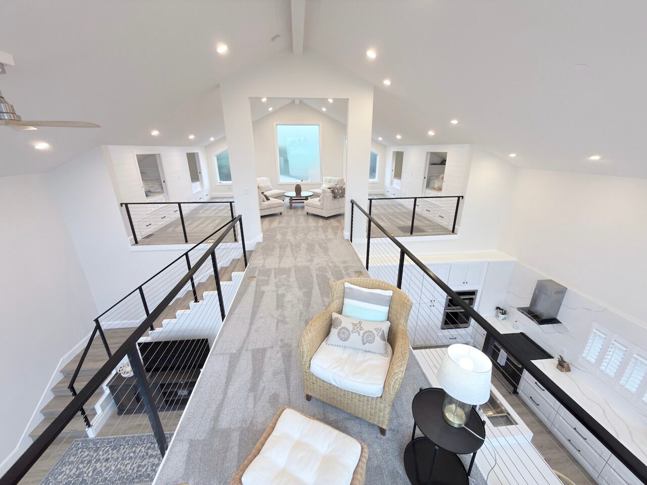 Ein großzügiges Loft-Apartment mit einer zentralen Treppe, einer gemütlichen Sitzecke mit Korbsessel und Kissen, einer Küche mit modernen Geräten und großen Fenstern mit Blick auf die Stadt.