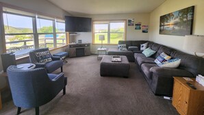 Un salon comprenant un canapé, un pouf et un fauteuil, un téléviseur à écran plat et une vue sur un lac.