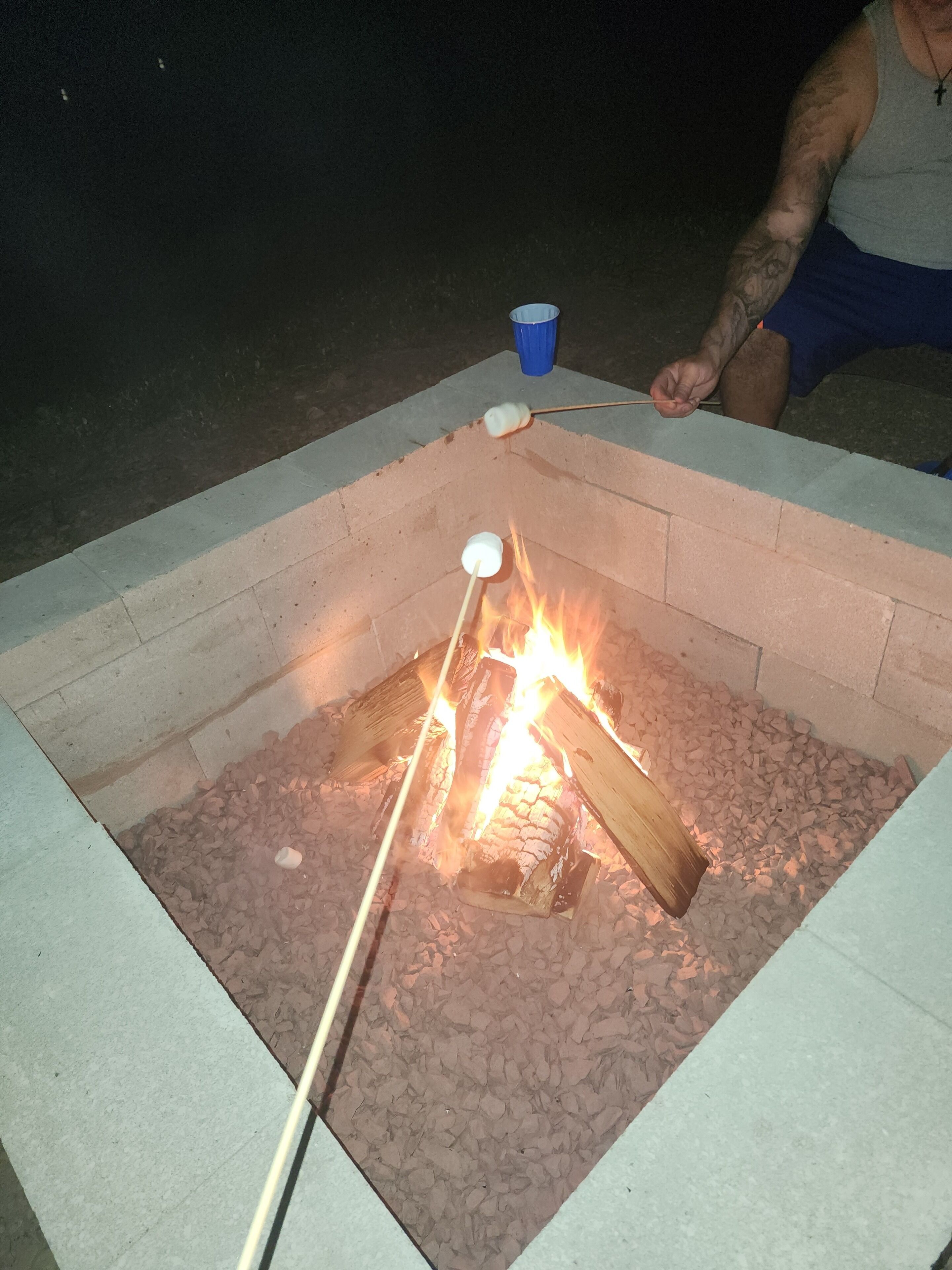 Ein Lagerfeuer mit Holzscheiten und einem Marshmallow am Spieß.
