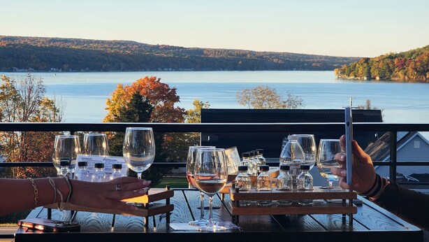 Une table dressée avec des verres et des bouteilles de vin, donnant sur un lac aux couleurs automnales.