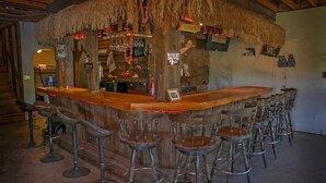 Un espace bar doté d’un toit de chaume, d’un comptoir en bois et de plusieurs tabourets.