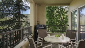 Ein Balkon mit Grill, einem runden Tisch und Stühlen sowie Blick auf Bäume.