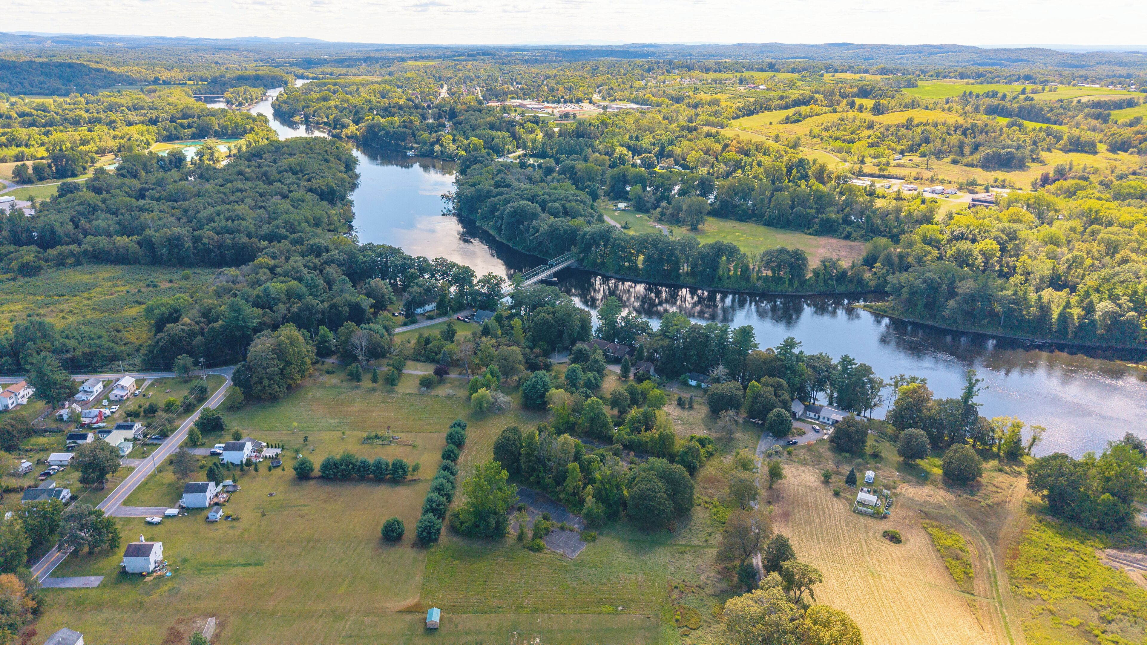 An aerial view of a riverside area with a bridge, houses, and greenery.