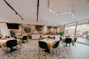 A modern dining area with tables and chairs, a kitchen counter, and a large window with a view of the outside.