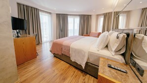 Quarto de hotel com uma cama grande, escrivaninha com televisão de tela plana e minibar.