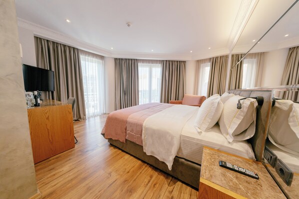 A hotel room with a large bed, a desk with a flat-screen TV, and a minibar. - Moenia Boutique Hotel (Durrës)
