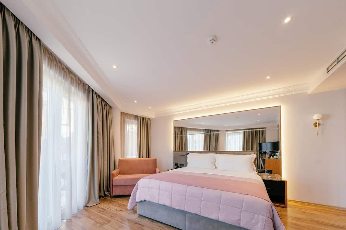 Une chambre d’hôtel moderne dotée d’un grand lit, d’un coin salon, d’une télévision et d’un miroir.