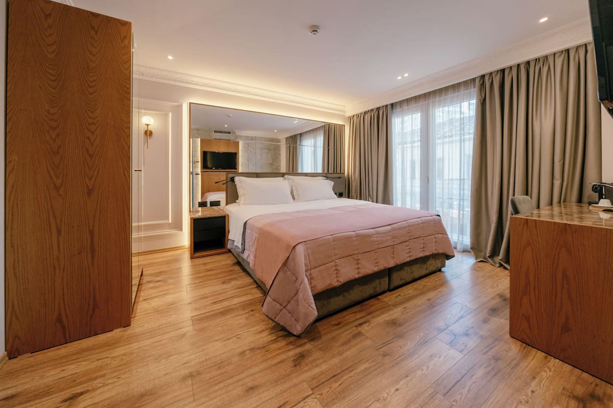 Une chambre d’hôtel moderne avec un grand lit, un plancher en bois, un bureau et une armoire.