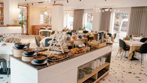 Buffet montado com diversos alimentos e uma área de estar com mesas e cadeiras.