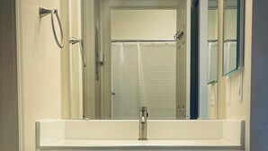 Un baño con tocador blanco, un espejo y cortina de ducha.