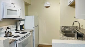 Una cocina con gabinetes blancos, microondas, refrigerador, estufa, cafetera y pileta.