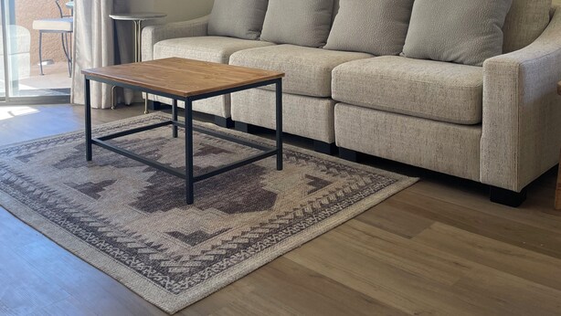 Una sala de estar con un sofá, una mesa de centro de madera y una alfombra estampada.