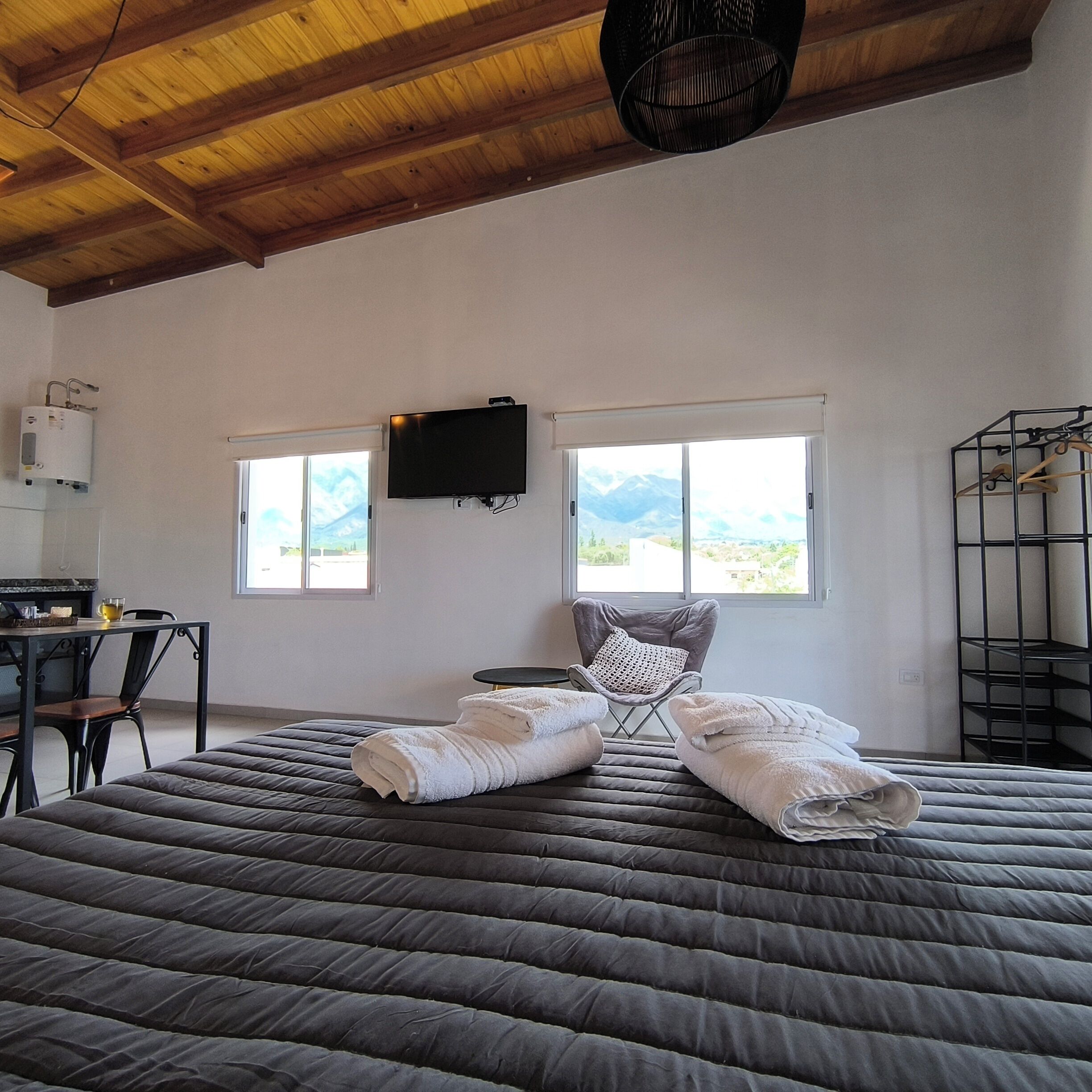 A bedroom with a large bed, a television mounted on the wall, and a view of mountains through the windows.